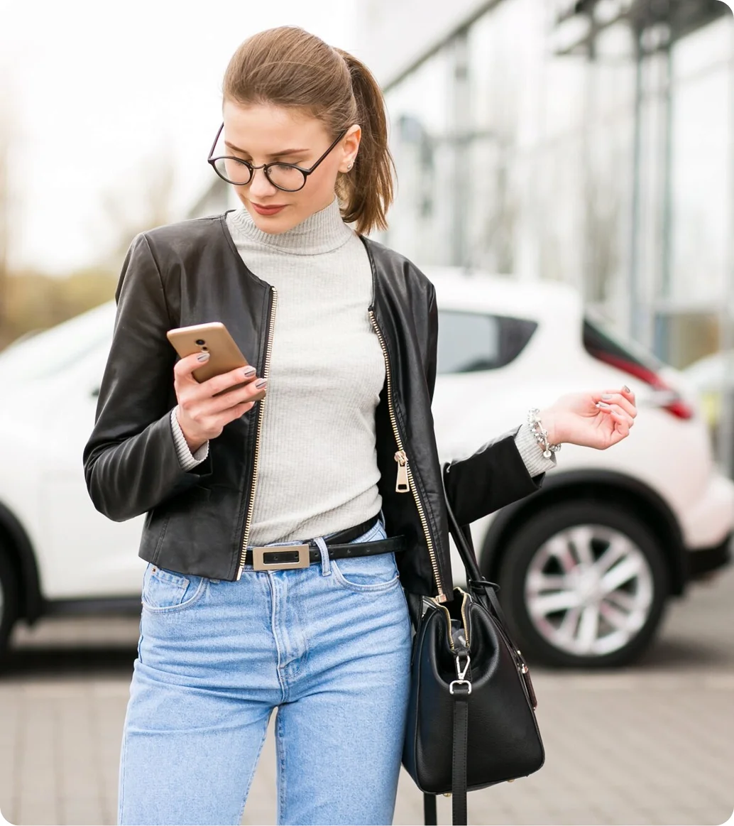 Nő mobiltelefonnal egy parkoló autó mellett